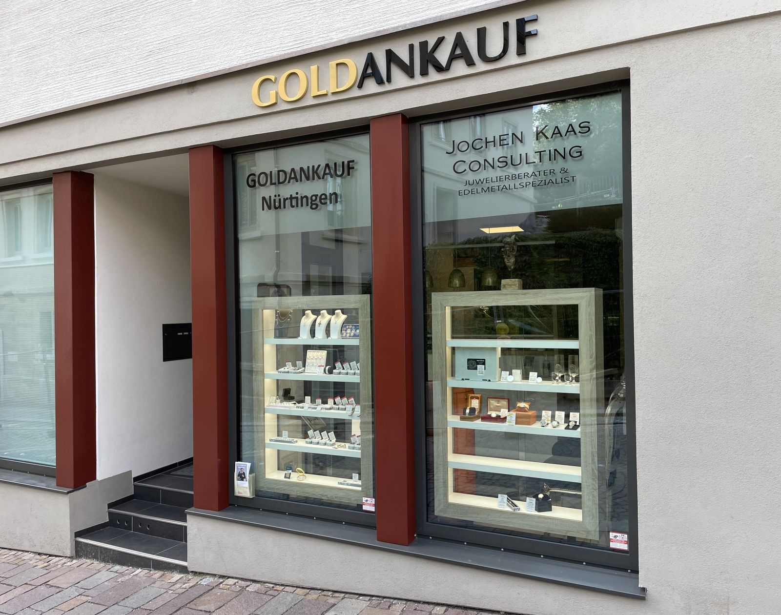 Ladenfront von vorn: der goldene Schriftzug Goldankauf über zwei Schaufenstern zwischen roten Pfeilern, links der Eingang mit Stufen